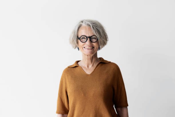 Portrait d’une femme senior confiante avec des cheveux courts portant des lunettes. Femme mûre souriante se tenant contre un mur blanc. Portrait d'une femme senior confiante avec des cheveux courts portant des lunettes. Femme mûre souriante se tenant contre un mur blanc.
